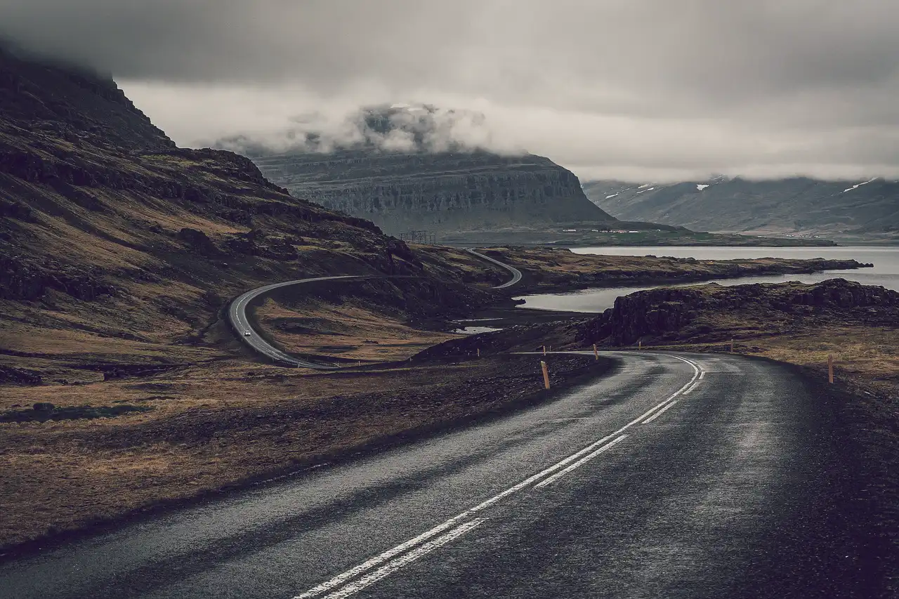 A desolate road disappearing into the distance and around a cloud topped mountain, symbolising the journey into the macabre and unknown and dark history
